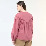 Blusa color rojo con escote en V y cuello mao. Presenta detalles de bordados tonales en el canesú delantero, mangas largas abullonadas y un diseño amplio y fluido.