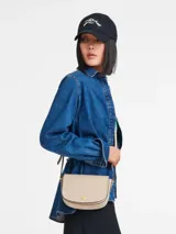 Cartera crossbody Longchamp de la línea Épure en tamaño S, color beige claro con bordes negros contrastantes. Cuenta con una solapa frontal redondeada, cierre con broche metálico dorado y correa ajustable para el hombro.