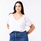 Remera blanca con cuello en V y mangas cortas adornadas con detalles bordados tipo broderie y perforaciones geométricas.