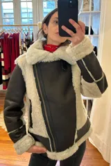 Campera tipo gamulán de cuero genuino color marrón oscuro, con interior y detalles en piel sintética color crema. Presenta cierre frontal cruzado, bolsillos laterales con cierre y puños con borde de piel.