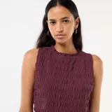 Top sin mangas de color bordó, confeccionado en tejido con textura fruncida. Presenta cuello redondo con detalle de volado y ruedo con terminación similar.