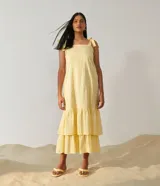 Vestido midi amarillo de algodón con tejido laise (ojales), escote cuadrado y tirantes ajustables con lazo. Presenta un diseño escalonado con volados en la falda.