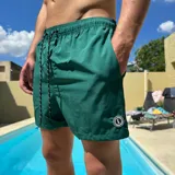 Short de baño negro con cintura elástica y cordón ajustable bicolor. Presenta un parche circular con logo en la parte inferior de la pierna.
