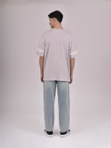 Remera gris de corte oversize con cuello redondo, mangas cortas con doble raya blanca y estampa frontal de una letra "W" grande en color blanco con efecto desgastado.
