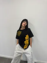 Remera negra de corte regular con estampado gráfico en color amarillo. Presenta inscripciones con estética oriental en la parte superior izquierda y en el lateral derecho. Confeccionada en algodón de alto gramaje con cuello reforzado y grifa de la marca en la manga.