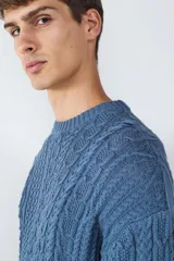 Sweater de punto color azul, con cuello redondo, manga larga y diseño de tejido a cables. Presenta detalles de cordones decorativos en el ruedo.