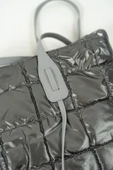 Cartera tipo shopper de color negro, con diseño acolchado y costuras cuadradas. Cuenta con doble asa larga para llevar al hombro y cierre superior.