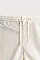 Short de baño en tejido técnico color beige claro, con cintura elástica ajustable con cordón y botón, bolsillos laterales y detalle de costuras en contraste.