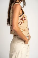 Chaleco de algodón color beige con estampado geométrico en tonos bordó y marrón. Presenta escote en V, cierre frontal con botones y corte recto.
