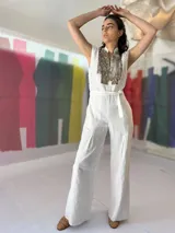 Mono largo color blanco, de lino con algodón, con bordado texturizado en los laterales superiores, cinto para ajustar en la cintura, cierre invisible central y bolsillos laterales.