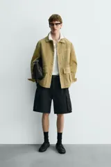 Cazadora de hombre de corte relajado, confeccionada en piel con acabado ante color mostaza/verde oliva. Presenta cuello solapa, manga larga con puño abotonado, cierre frontal de botonadura y cuatro bolsillos de plastrón visibles (uno en el pecho y tres en la parte inferior).