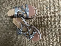 Sandalias de cuero color plata con tiras finas con nudos. Taco de madera y goma de 7cm de altura. Hechas a mano en Uruguay.