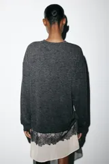 Vestido de cuello redondo y manga larga, confeccionado en tejido de punto gris oscuro. Presenta un bajo en contraste de color beige con detalle de encaje floral negro y lazada lateral ajustable.