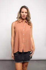 Blusa sin mangas color terracota, con cuello camisero y abotonadura frontal. Presenta un calce holgado y aberturas laterales en el ruedo.