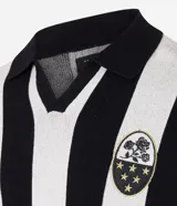 Sweater de punto con diseño de rayas verticales blancas y negras, cuello polo con escote en V y manga corta. Presenta un parche bordado en el pecho izquierdo con rosas y estrellas, y un estampado central con el texto "DISRUPT SPORTING CLUB".