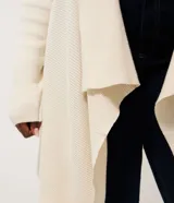 Cardigan de punto color marrón, con diseño alargado y puntas asimétricas. Presenta mangas largas, cuello tipo chal y detalles de textura canelada en los laterales.