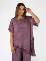 Blusa de viscosa color morado, con mangas cortas, cuello redondo y detalle de encaje en las terminaciones de las mangas y el ruedo asimétrico.