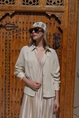 Camisa de lino negra con bordados dorados en forma de árbol o palmera estilizada. Presenta cuello camisero, botones frontales dorados y pliegues verticales en la parte inferior delantera.