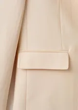 Blazer de diseño recto y estilo sastrero, color beige, confeccionado en mezcla de lyocell y poliéster. Cuenta con cuello en pico con solapas de muesca, manga larga, bolsillos delanteros con solapa y cierre frontal de un botón.