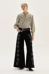 Jean de corte pata ancha color negro, con diseño de paneles frontales y bordados florales a lo largo de las piernas.