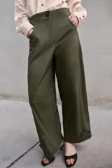 Pantalón de tiro alto en color verde militar, con corte barrel de pernera holgada que se estrecha hacia el tobillo. Presenta trabillas laterales ajustables en la cintura y en el bajo, bolsillos delanteros y cierre frontal con cremallera y botón.
