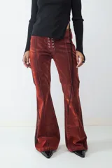 Pantalón de denim con acabado flocked que le otorga una textura aterciopelada, de tiro medio y corte flare. Presenta un cierre frontal con cordones y ojales metálicos, costuras verticales decorativas y paneles laterales en contraste.