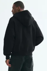 Campera canguro de felpa negra con capucha ajustable, cierre frontal completo y bolsillos tipo parche, de corte oversized.
