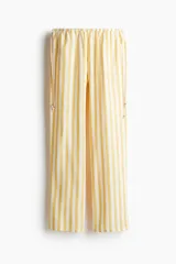 Pantalón de corte holgado y piernas anchas, con estampado de rayas verticales en tonos amarillo y blanco. Presenta cintura elástica con cordones laterales ajustables decorados con cuentas en los extremos y bolsillos laterales.
