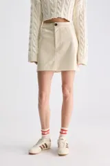 Minifalda evasé de material sintético color beige, con tiro alto y cierre frontal con botón.