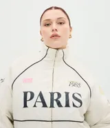 Campera bomber oversized de microfibra color beige, con cierre frontal por cremallera, cuello alto y bolsillos delanteros. Presenta estampado frontal con la inscripción "PARIS 1985" en color negro, además de detalles estampados en las mangas. Cuenta con puños y ruedo elásticos.