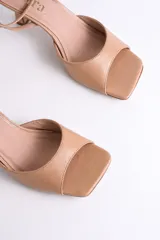 Sandalia de vestir color nude, con punta cuadrada, tira ancha sobre los dedos y pulsera al tobillo con hebilla dorada.