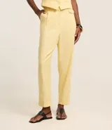 Pantalón zanahoria de tiro alto color amarillo pálido, confeccionado en viscolino con 15% de lino, con trabillas en la cintura, solapas con botón abajo de la cintura, pliegues y cierre tradicional.