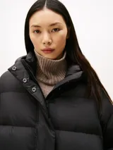 Campera acolchada tipo puffer de Tommy Hilfiger, color negro, con relleno de plumón, capucha fija, cierre frontal con cremallera oculta y botones a presión, y logo tonal bordado en el pecho.