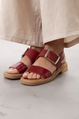 Sandalias de cuero marrón, con diseño de dos fajas amplias, una lisa en la parte delantera y otra superior con hebilla metálica grande y ajustable. Suela plana con plataforma baja y pespunte visible.