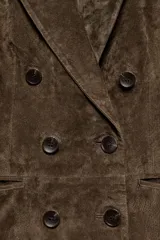 Blazer de ante color marrón, con cuello solapa, hombreras, manga larga y cierre frontal cruzado con botones. Cuenta con bolsillos delanteros de doble vivo.