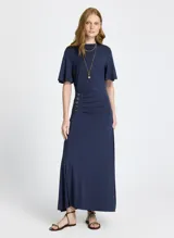 Vestido largo azul marino de punto ligero, con escote redondo, mangas cortas, abertura lateral y detalle de botones dorados en el lateral.