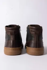 Championes de caña alta confeccionados en cuero marrón oscuro, con cordones al tono y suela de goma color caramelo.