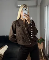 Campera tipo bomber confeccionada en gamuza, con cierre frontal metálico y detalle de flores bordadas en relieve en el frente.