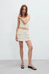 Falda pantalón satinada de tiro medio y color negro, con bolsillos cargo de plastrón con solapa, pliegues decorativos en el delantero y cierre lateral con cremallera oculta.