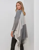 Ruana tejida con diseño colorblock en tonos de gris y beige, con flecos en el borde inferior.