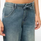 Pantalón de jean con corte baggy y pierna ancha, de tiro medio con cintura elástica ajustable mediante cordón. Presenta un lavado desgastado en tono azul medio.