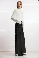 Pantalón de tiro alto efecto piel en color marrón, con pierna ancha y costuras marcadas en la parte delantera. Presenta trabillas en la cintura y cierre frontal con cremallera, botón y gancho metálico.