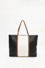 Cartera tipo tote bag en símil cuero, con diseño en bloques de color negro y blanco, y detalles en marrón. Tiene asas largas para llevar al hombro y un cierre magnético.