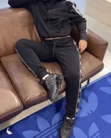Pantalón de jogging negro, de corte regular con puños elásticos y cintura ajustable con cordón. Cuenta con bolsillos laterales con cierre y bandas laterales personalizadas con inscripciones.