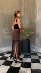 Falda corta tejida a mano en crochet, con diseño a rayas horizontales en tonos marrón oscuro y dorado brillante. Presenta un borde inferior con flecos largos y abundantes.