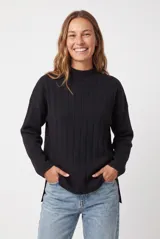 Buzo de punto negro, de corte holgado y largo amplio, con cuello alto acanalado y mangas largas.