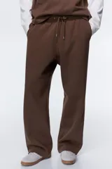 Pantalón deportivo de felpa marrón con elástico en la cintura, cordón de ajuste y bolsillos laterales, corte holgado.