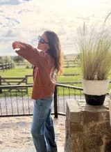 Campera bomber de jean color terracota, con corte holgado. Presenta apliques de cuero cortados y bordados a mano en la espalda, delantera y cuello, formando un diseño de montañas en tonos beige, rosa y verde militar.