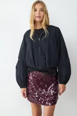 Campera de nailon negra con cuello redondo, cierre frontal de cremallera metálica, mangas largas abullonadas con puños elásticos y bajo fruncido.
