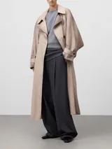 Gabardina cruzada color beige con efecto envejecido, de corte recto y largo midi. Presenta doble solapa en el lado derecho, doble botonadura frontal, bolsillos laterales, mangas largas con trabillas en los puños y canesú amplio en la espalda.